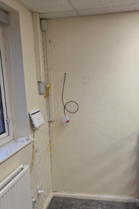 The office corner before installation - bare wall with loose cabling and conduit where the network cabinet will go